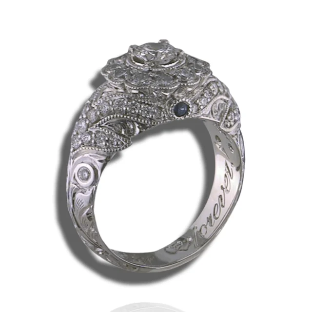 Floral diamond cluster ring with engraved leaf-like scrolls, beaded edges and a small dark blue stone below the setting.